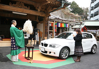 A person receiving a prayer from the priest and the car her owns.